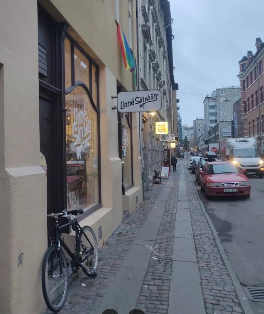 Linné Skivbörs skylt upplyst i skymningen längs Andra Långgatan, med kullerstensgatan och cyklar utanför